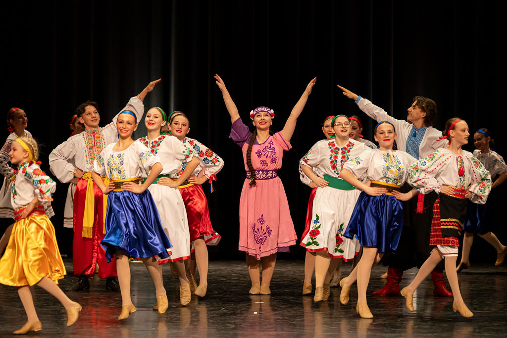 Boyan dancers in vibrant, traditional Ukrainian costumes perform joyfully on stage. They wear embroidered dresses and skirts, conveying energy and celebration.