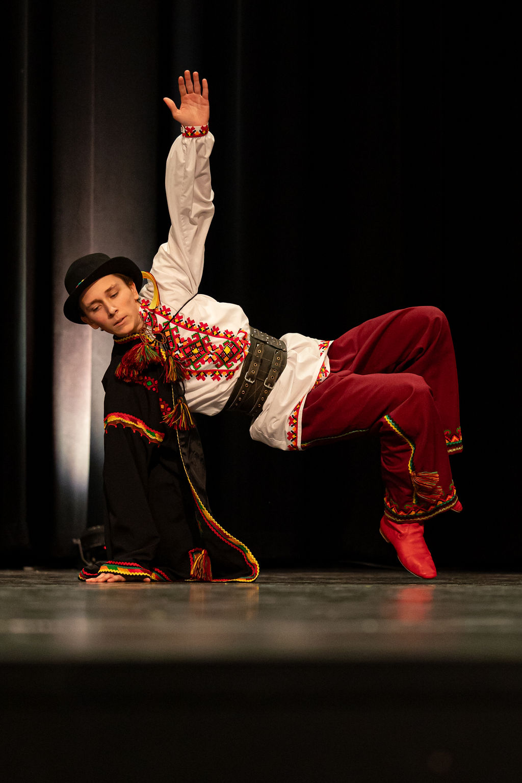 A Boyan dancer in traditional Ukrainian attire, featuring embroidered shirt and red pants, performs a dynamic move on stage, conveying grace and concentration.