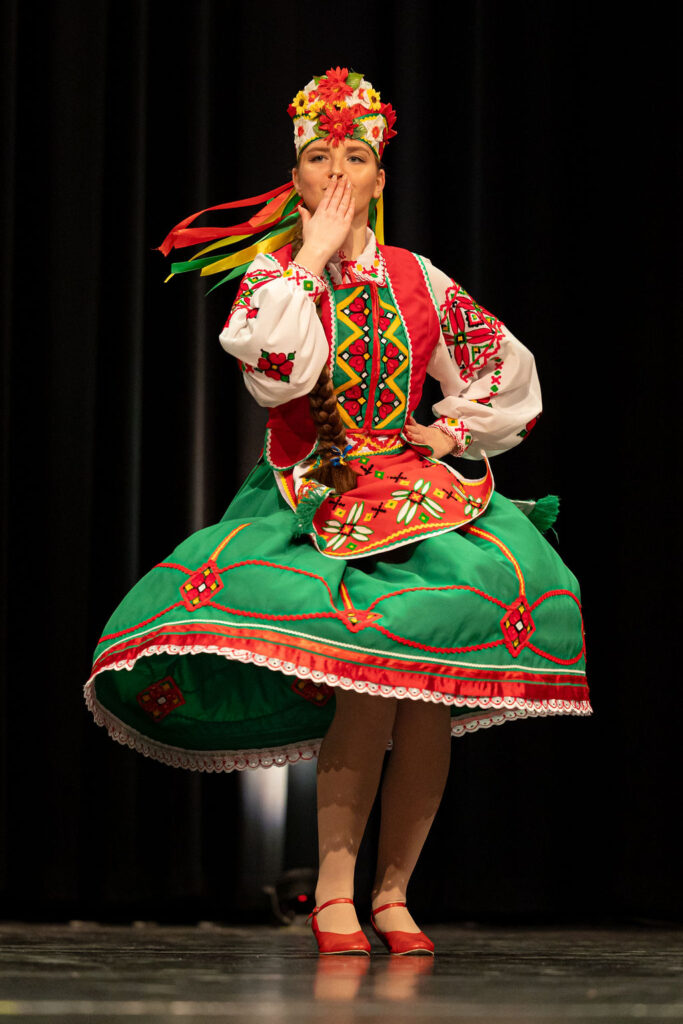 Boyan Dance Recital 2025 A Boyan Dance dancer in vibrant Ukrainian folk attire, with a floral headpiece and colorful ribbons, sends a kiss while performing on stage, exuding joy and cultural pride.
